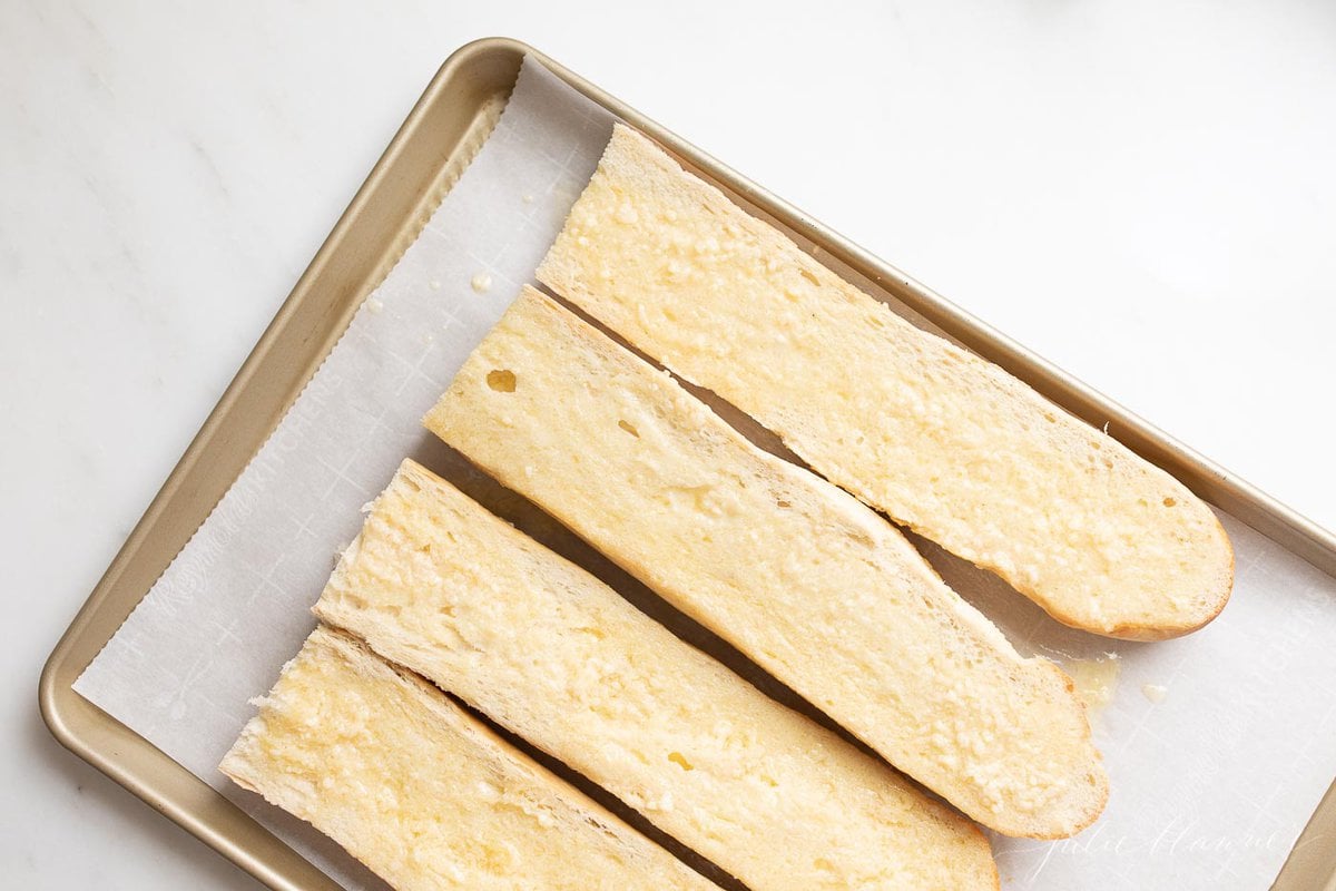 Bread, sliced open on a parchment lined baking sheet.