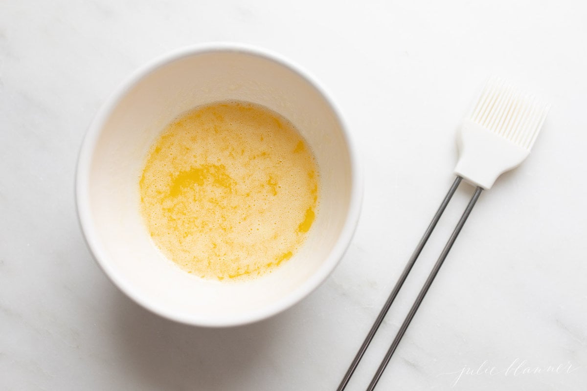 Melted butter in a white bowl with a basting brush next to it.