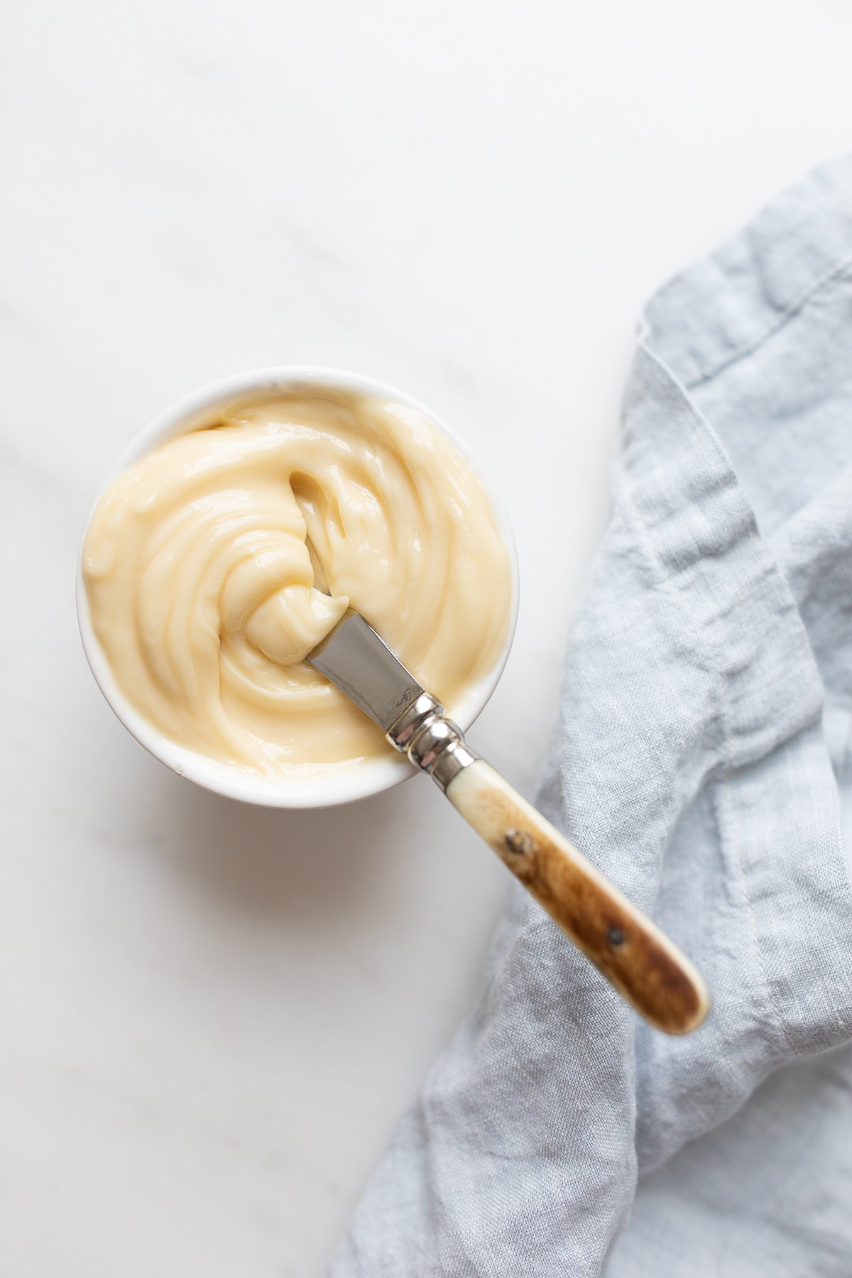 A small white bowl full of honey butter, knife and blue linen napkin to the side.