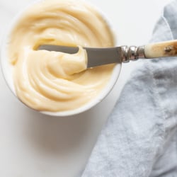 A small white bowl full of honey butter, knife and blue linen napkin to the side.