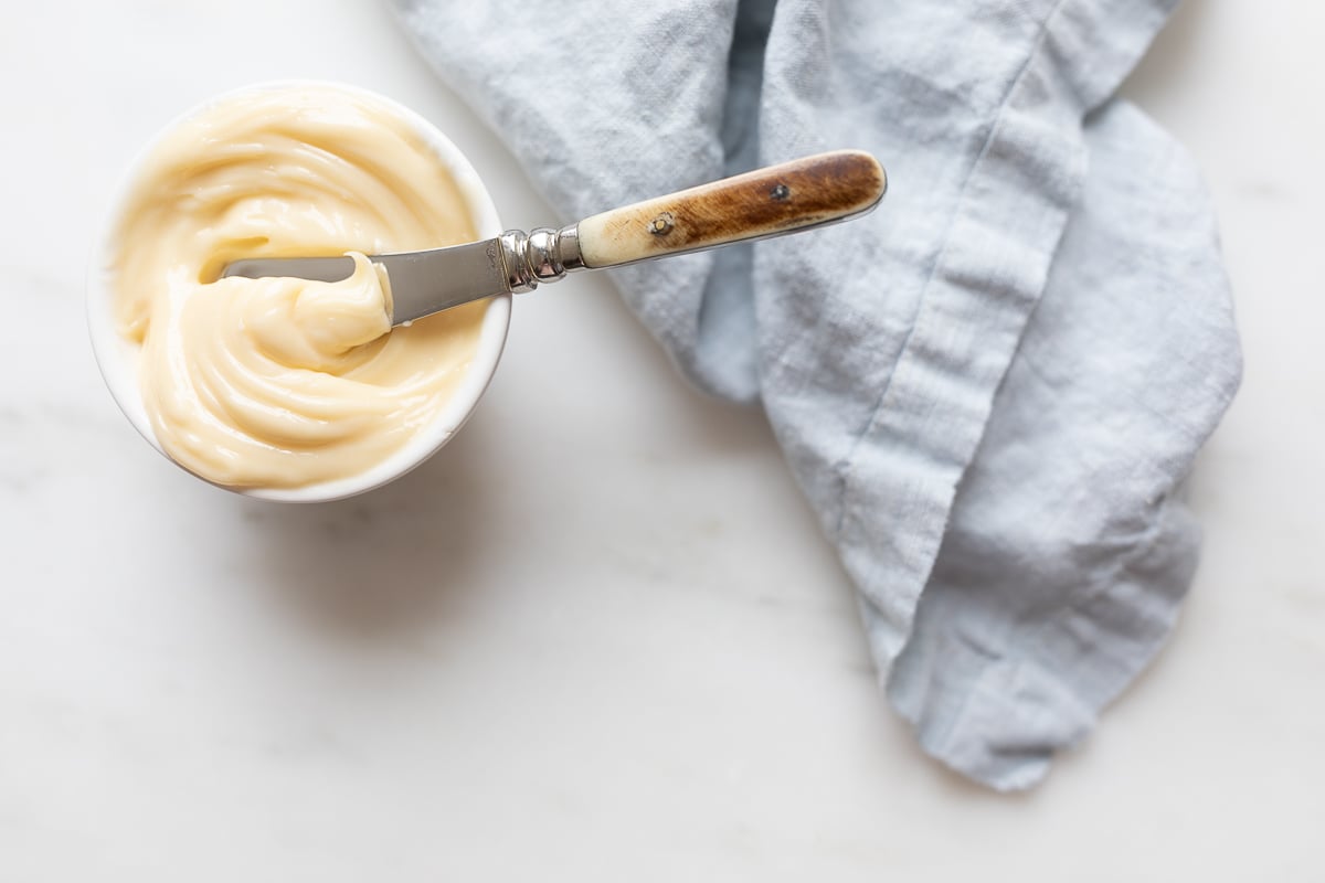 A small white bowl full of honey butter, knife and blue linen napkin to the side.