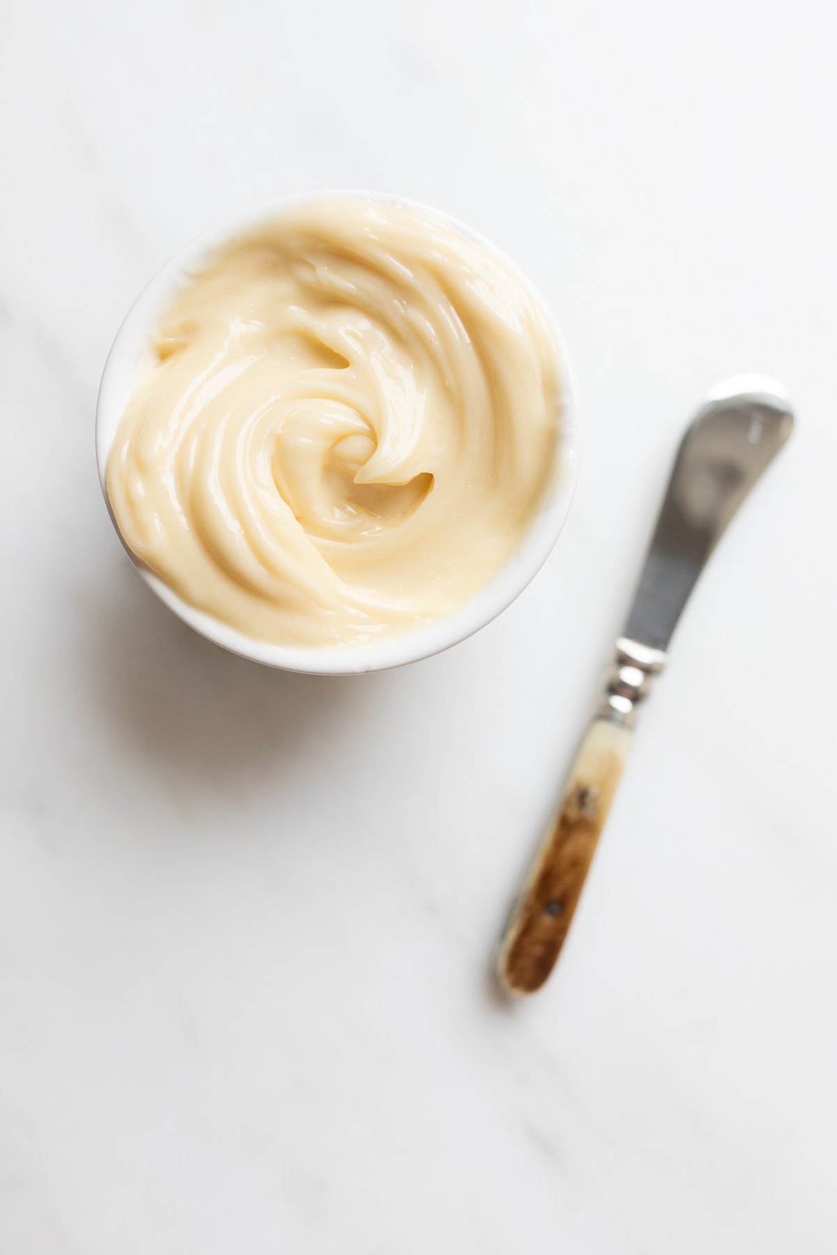 A small white bowl full of honey butter, knife to the side.