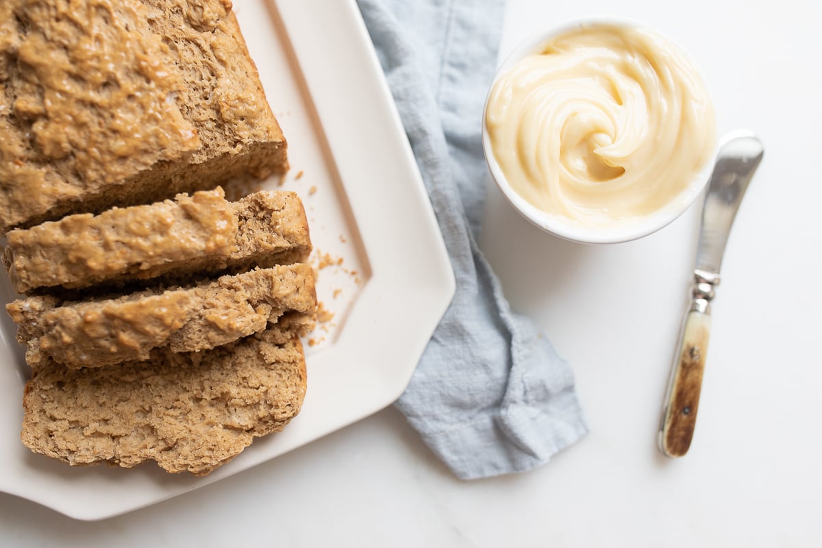 A loaf of sliced bread next to a bowl of honey butter and a spreading knife.