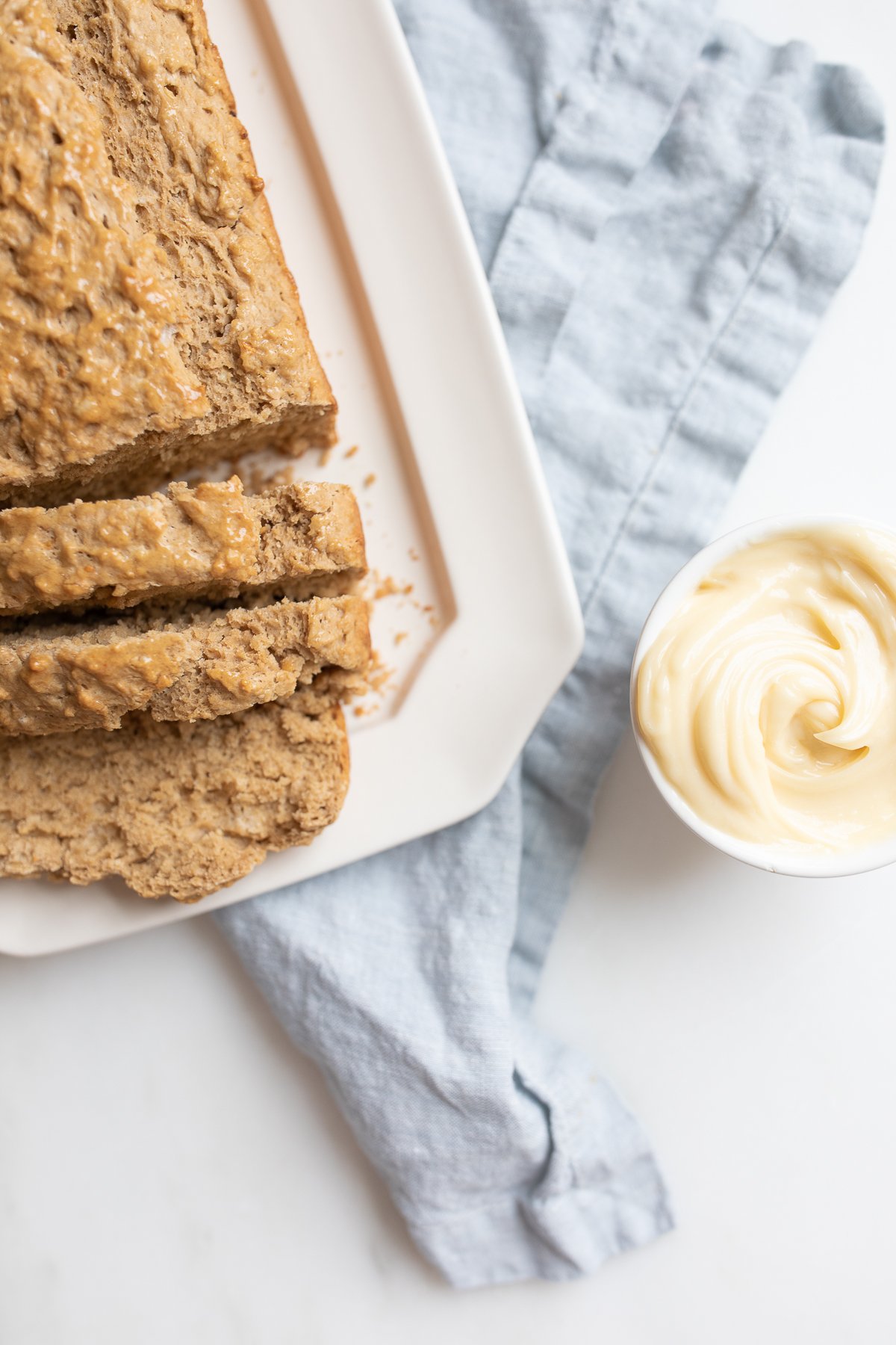 A loaf of sliced bread next to a bowl of honey butter and a spreading knife.