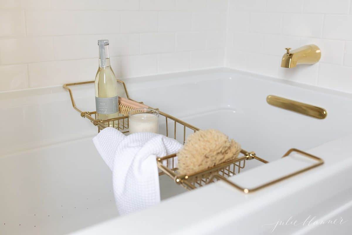 A brass bath tray with various items like a candle, champagne, sponge, and a wash cloth to make the ultimate bath experience. 