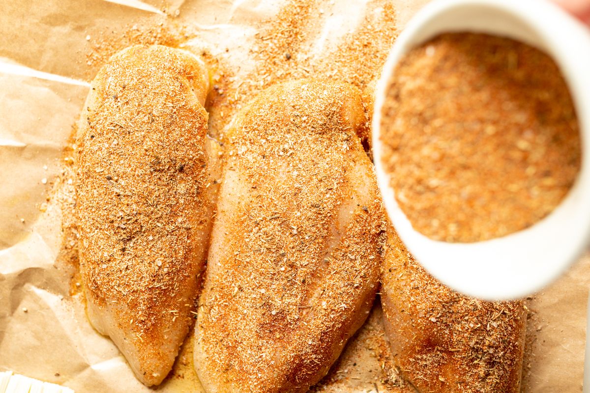 Raw chicken breasts on butcher paper, with butter and seasonings