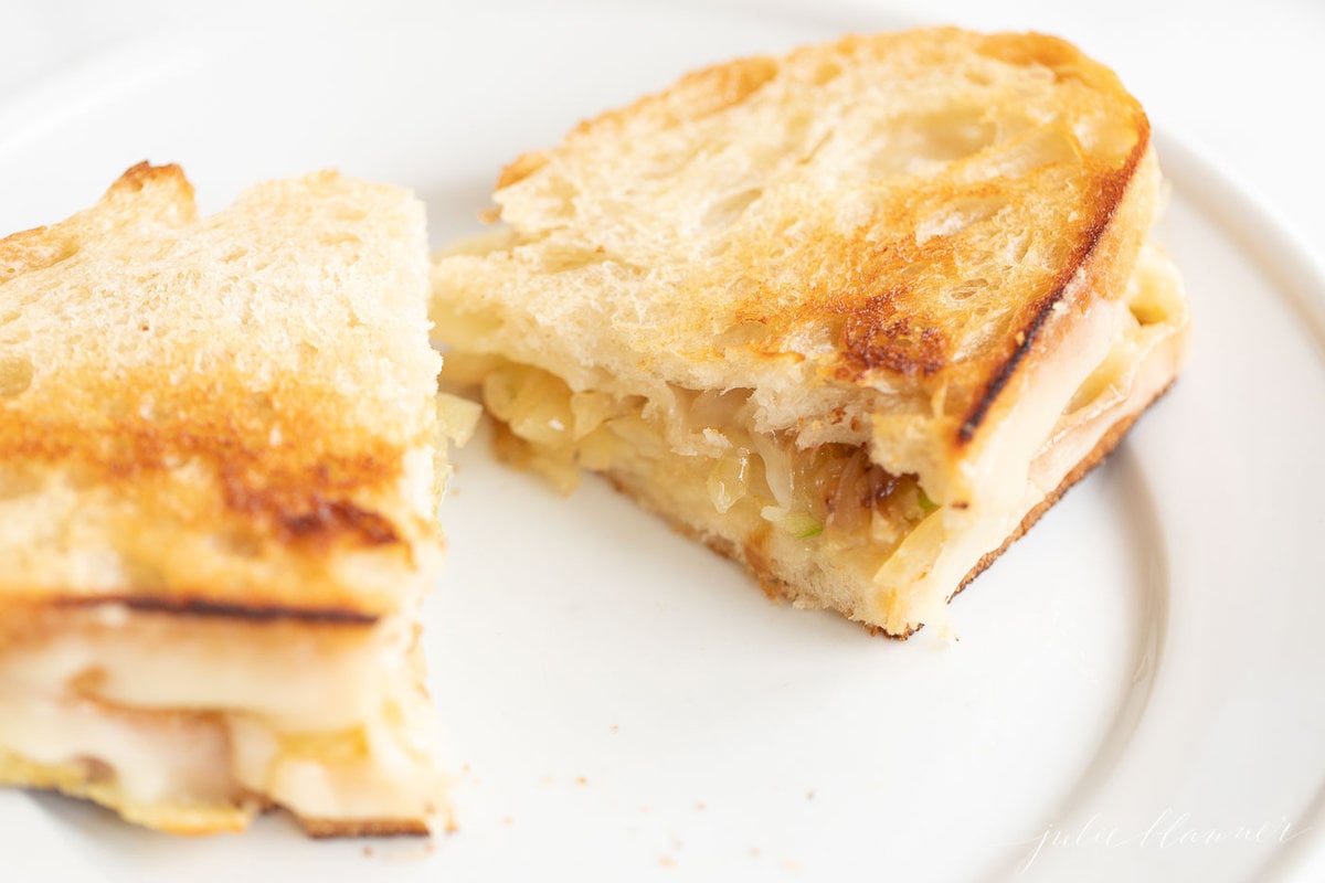 A white plate with a gourmet grilled cheese cut in half.