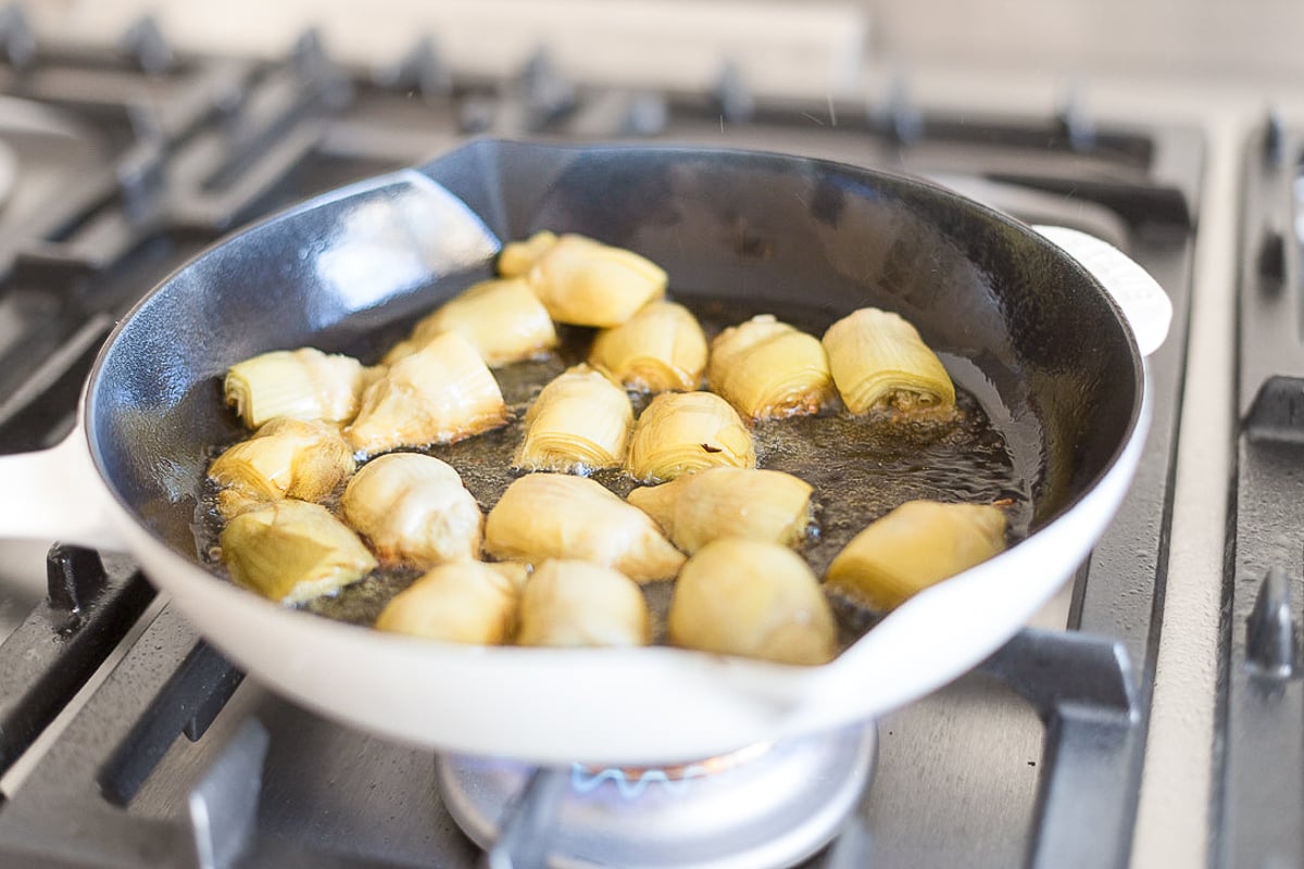 Artichokes in a saute pan on a stovetop.