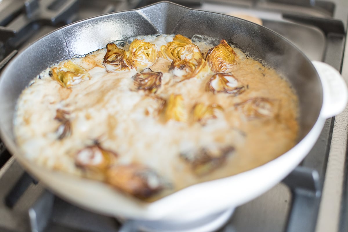 Fried artichokes in a saute pan on a stovetop.