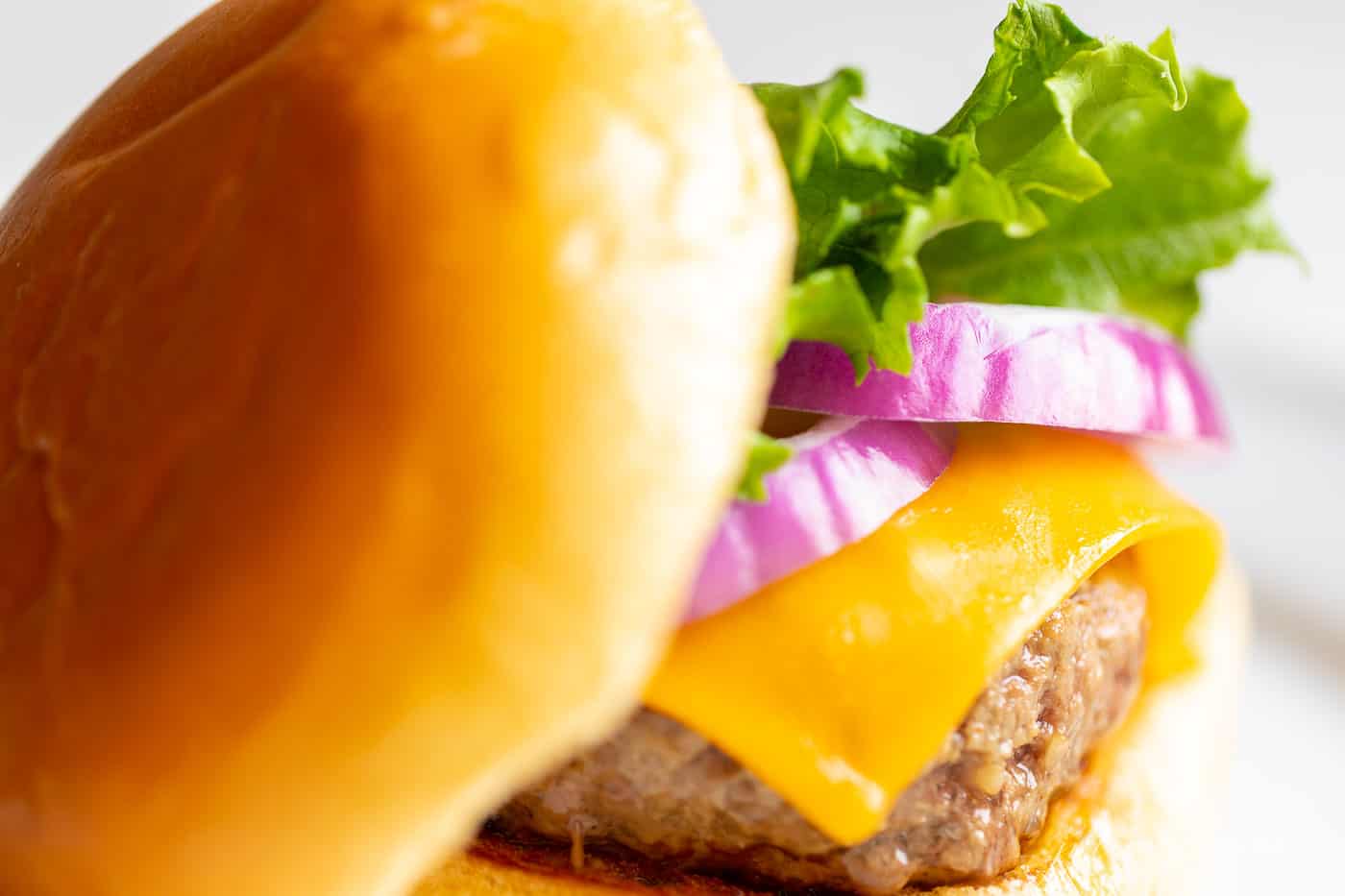 A juicy burger with lettuce, cheese, and onions on a white plate. 