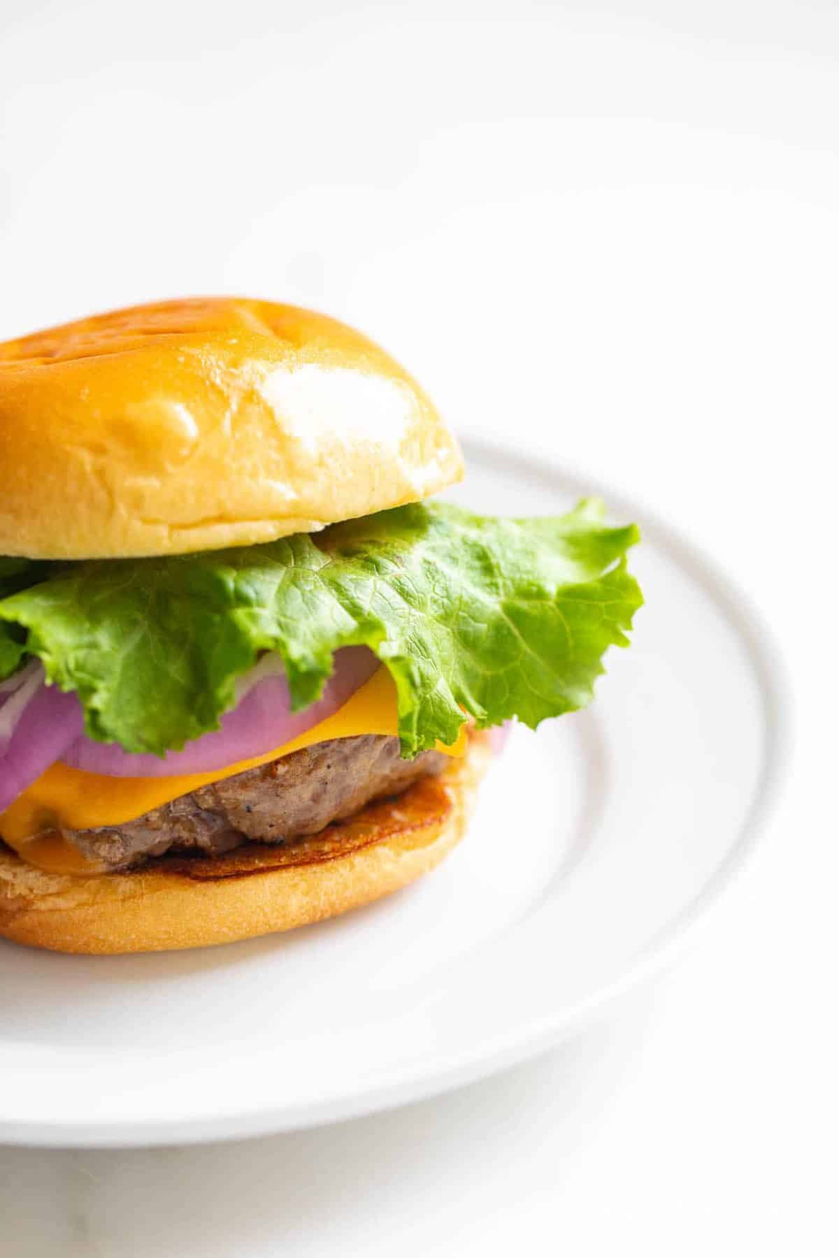 A juicy burger with lettuce, cheese, and onions on a white plate. 