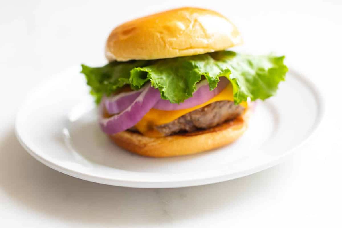 A juicy burger with lettuce, cheese, and onions on a white plate. 