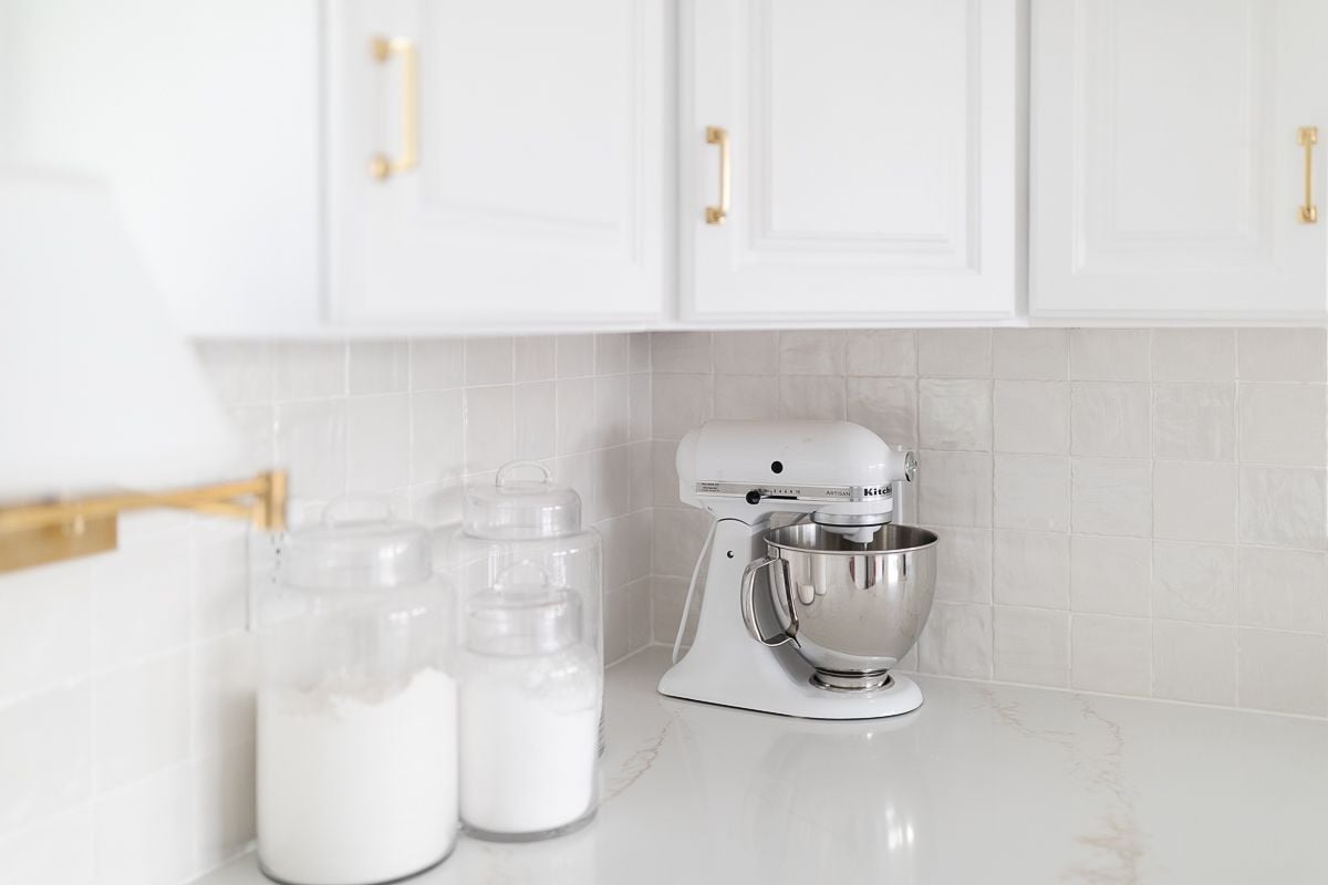 A white kitchen with glass flour and sugar canisters and a white kitchenaid mixer for kitchen counter organization