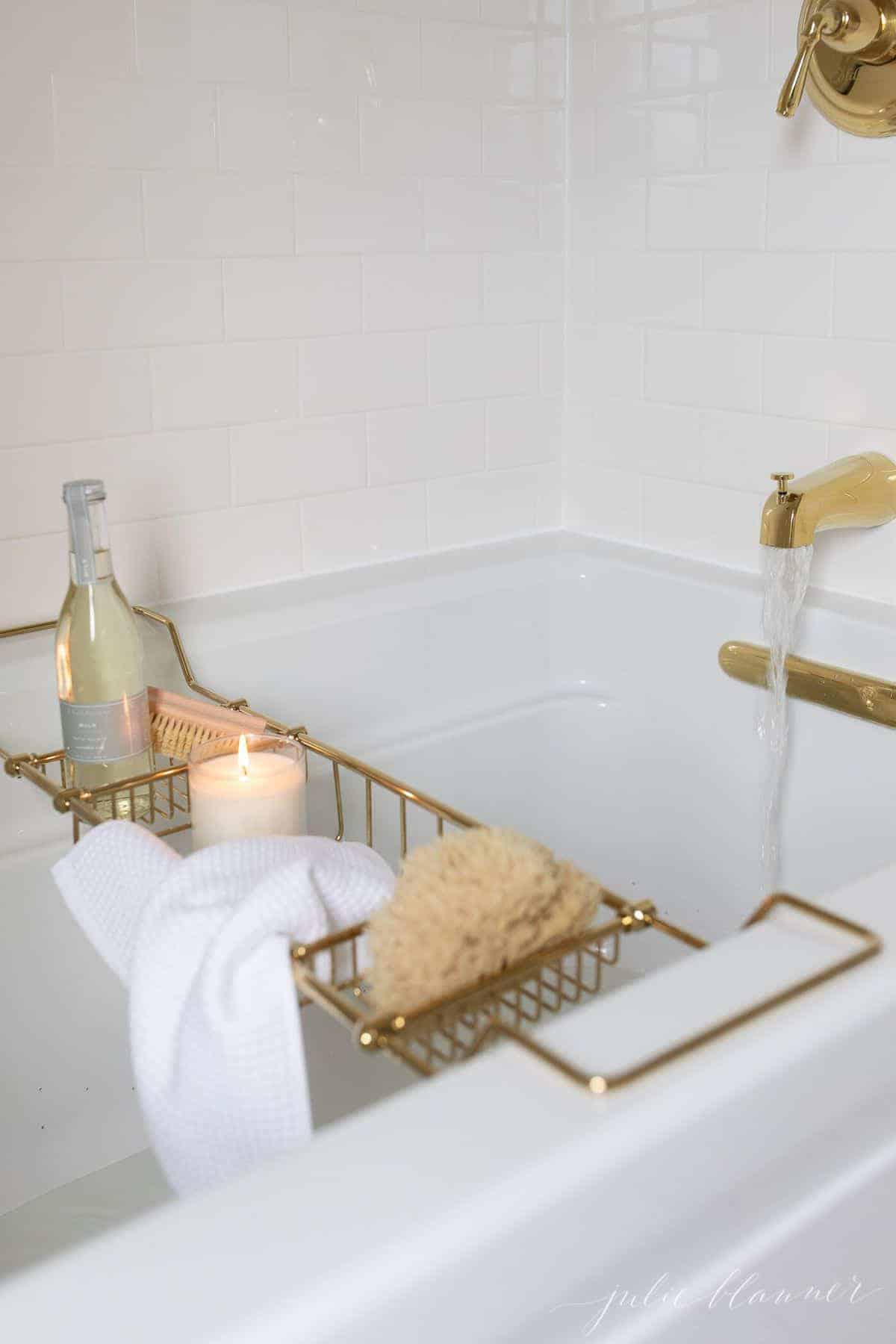 A brass bath tray with various items like a candle, champagne, sponge, and a wash cloth to make the ultimate bath experience. 