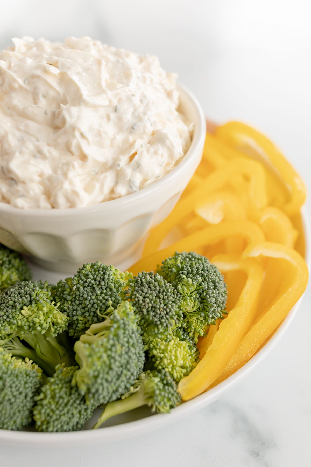 A white bowl full of veggie dip, surrounded by cut vegetables.