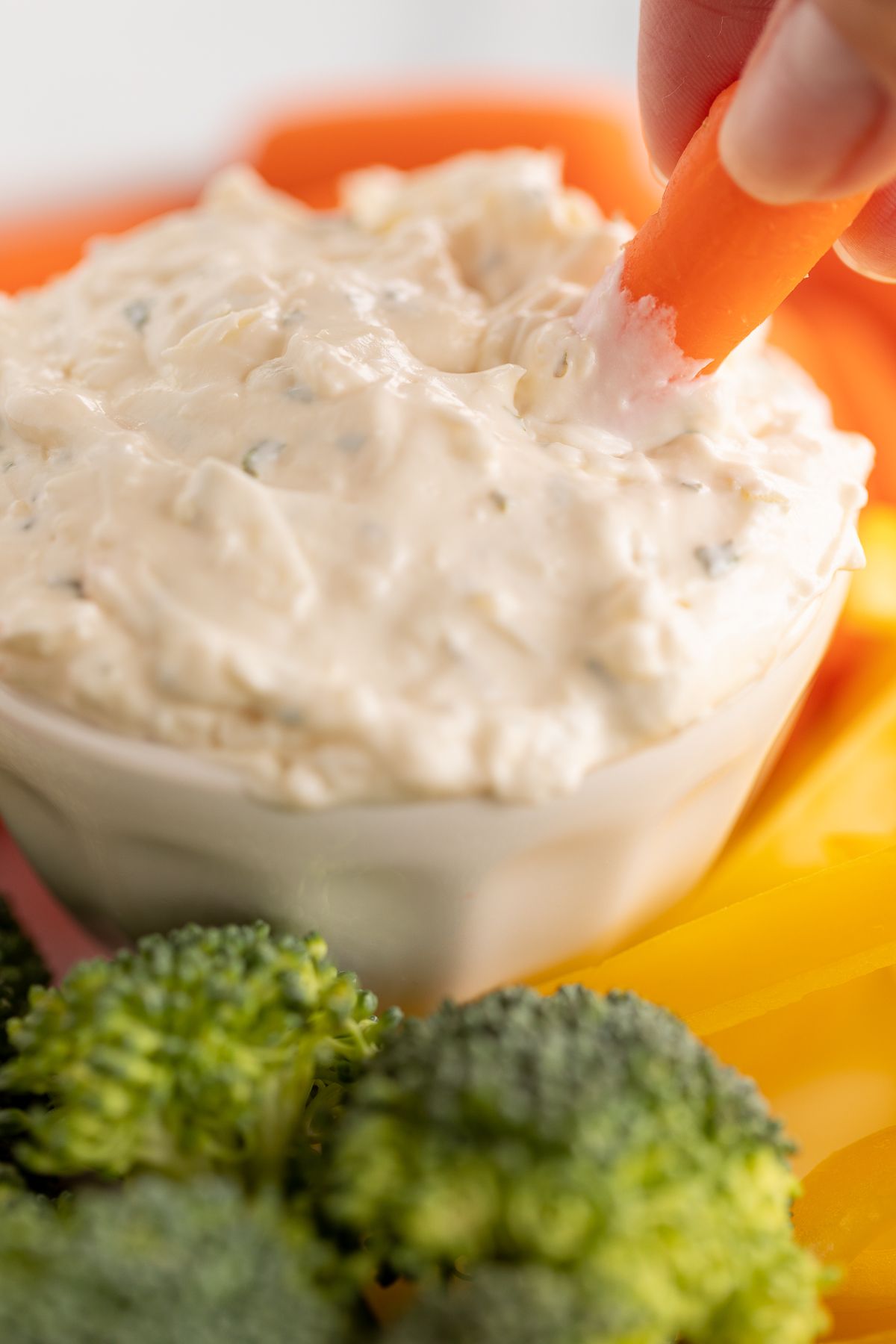 A white bowl full of vegetable dip, surrounded by cut vegetables.