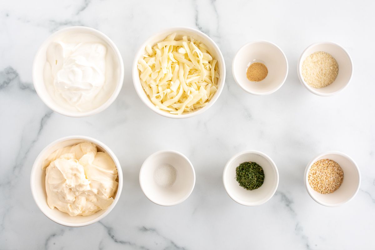 Ingredients for vegetable dip, in small white bowls on a marble surface.