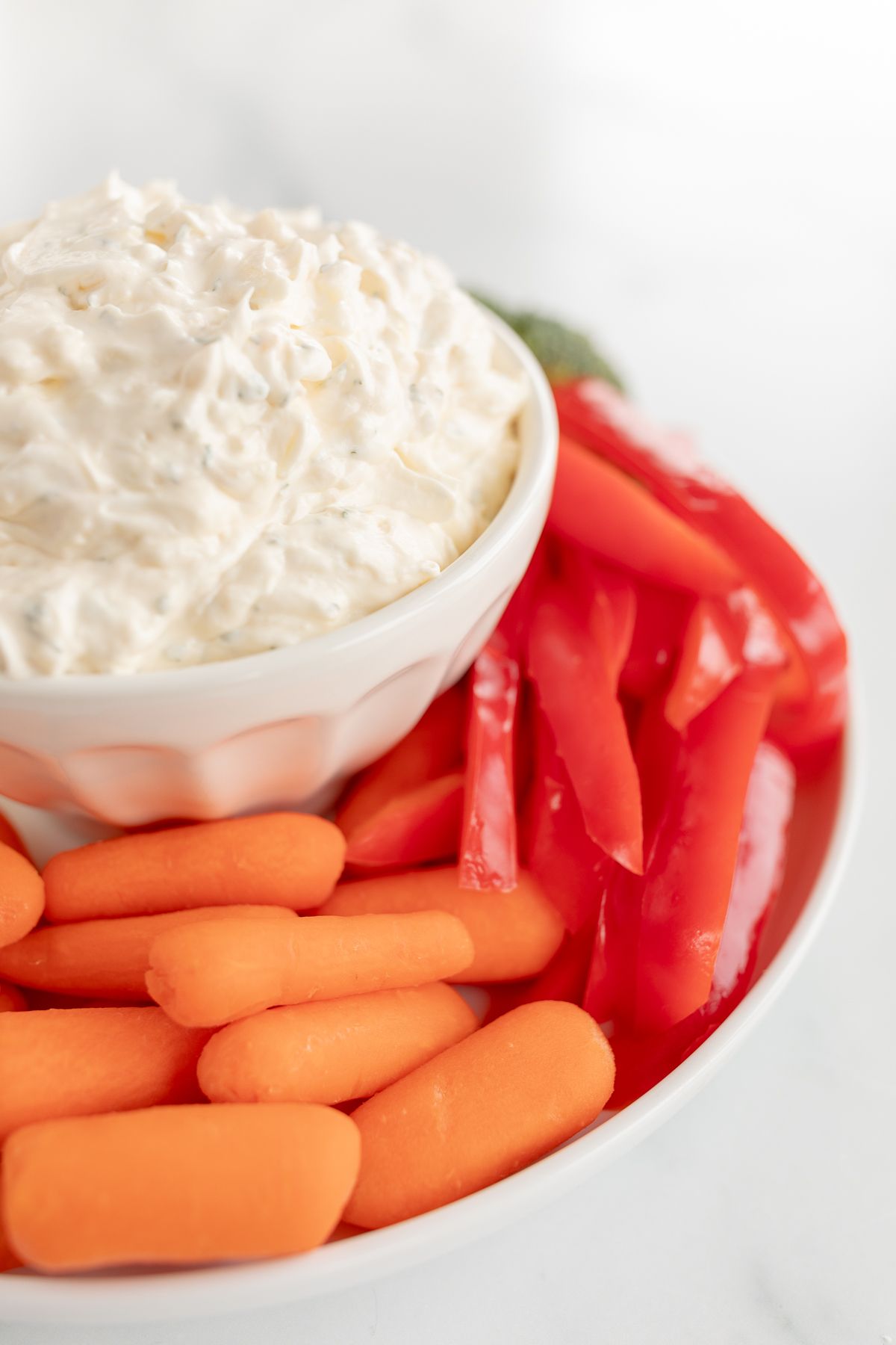 A white bowl full of veggie dip, surrounded by cut vegetables.