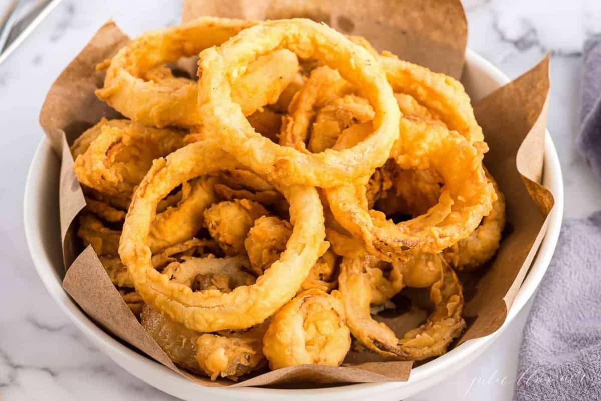 A white bowl of homemade onion rings, butcher paper lining the bowl.