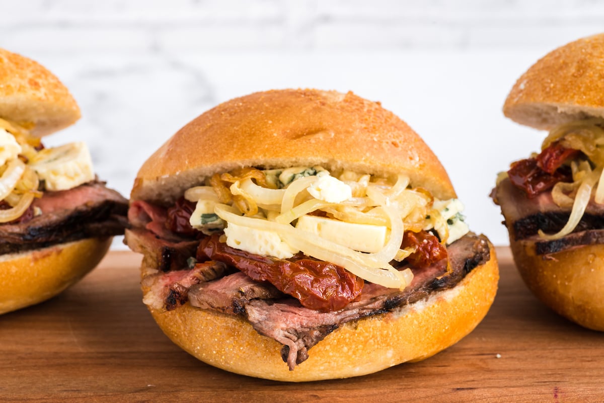 A steak sandwich with onions on a wooden surface.