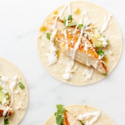Chicken tacos in corn tortillas on a white surface.