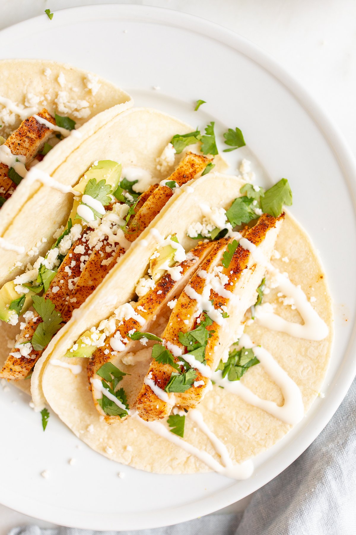 Chicken tacos in corn tortillas on a white surface.