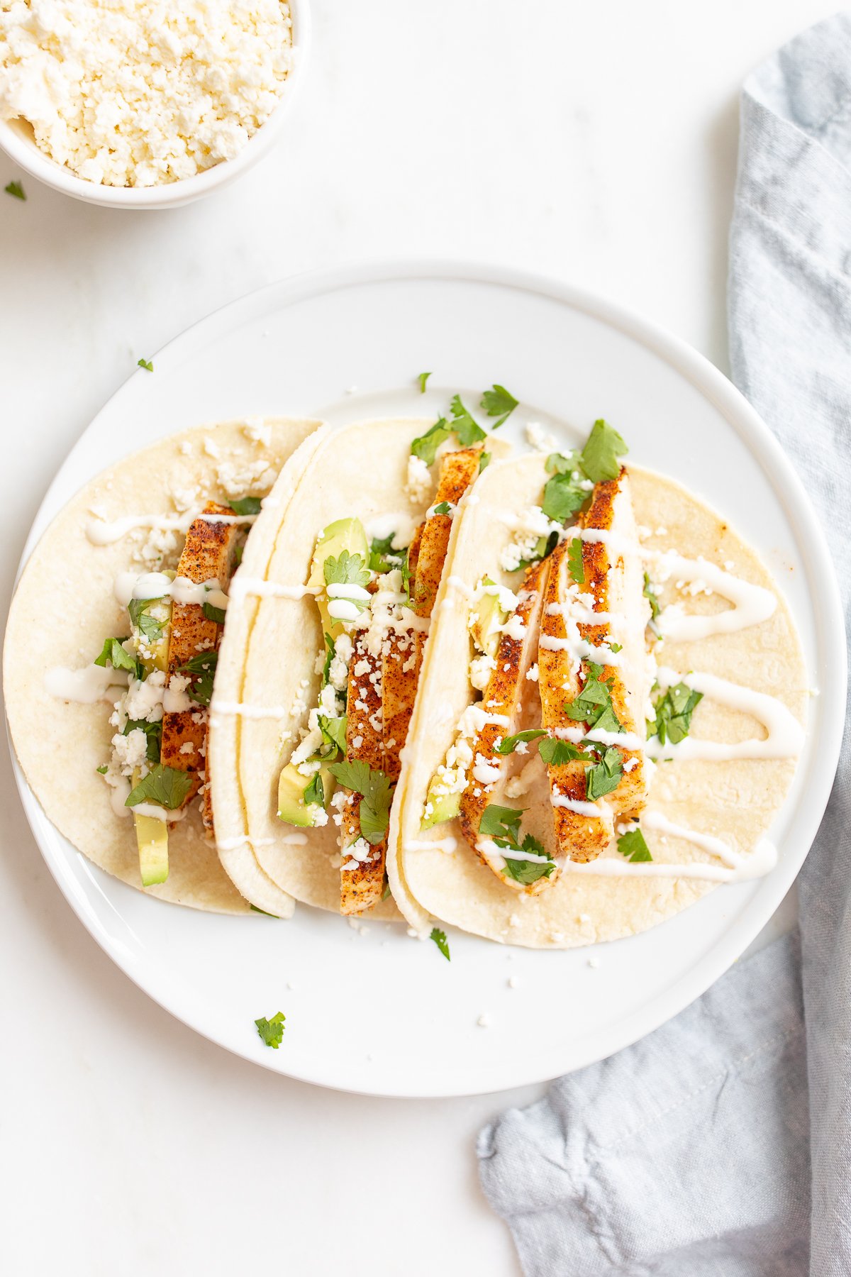Chicken tacos in corn tortillas on a white surface.