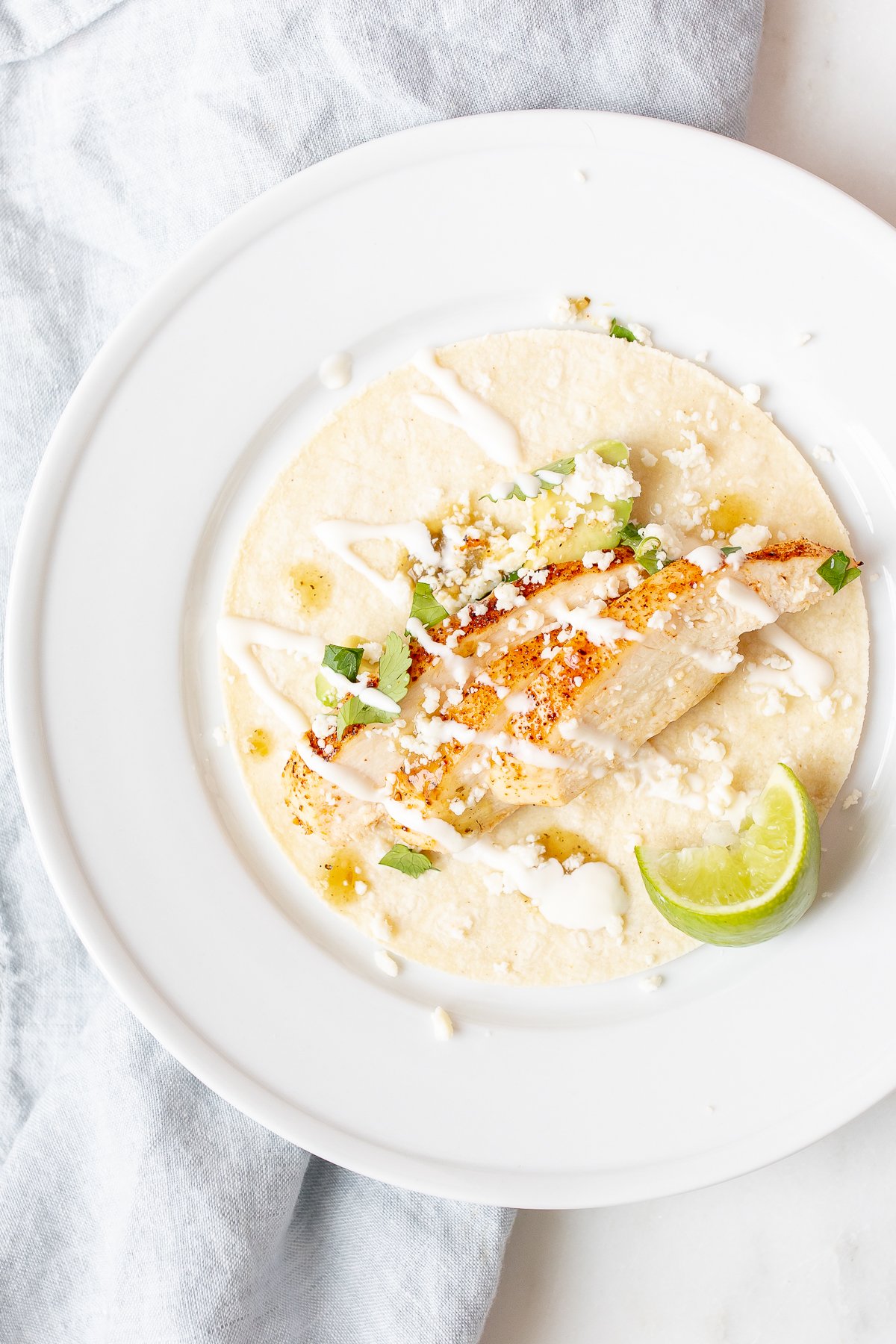 Chicken soft tacos in corn tortillas on a white surface.