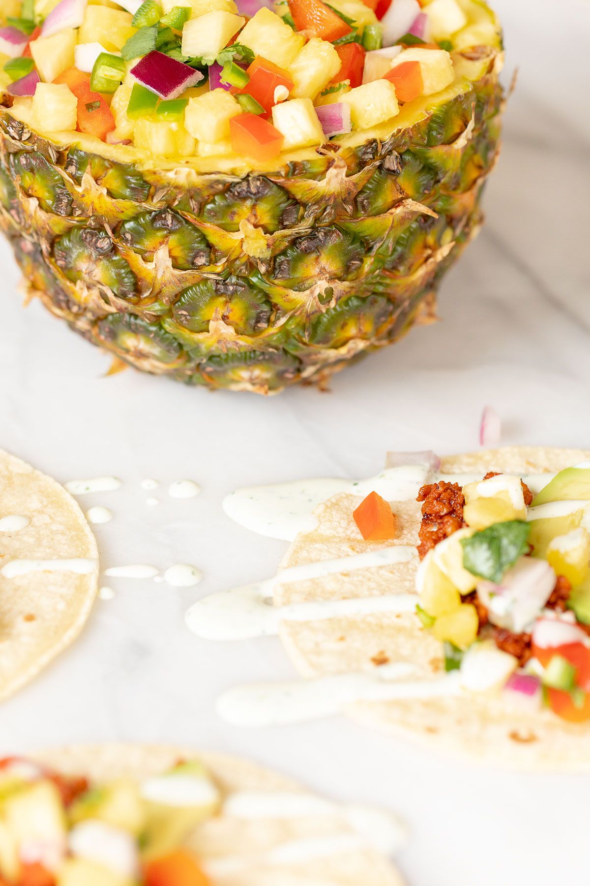 Chorizo tacos topped with avocado, pineapple and lime crema. Pineapple full of salsa in the background