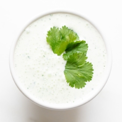 A white bowl of crema de cilantro on a white countertop, garnished with cilantro.