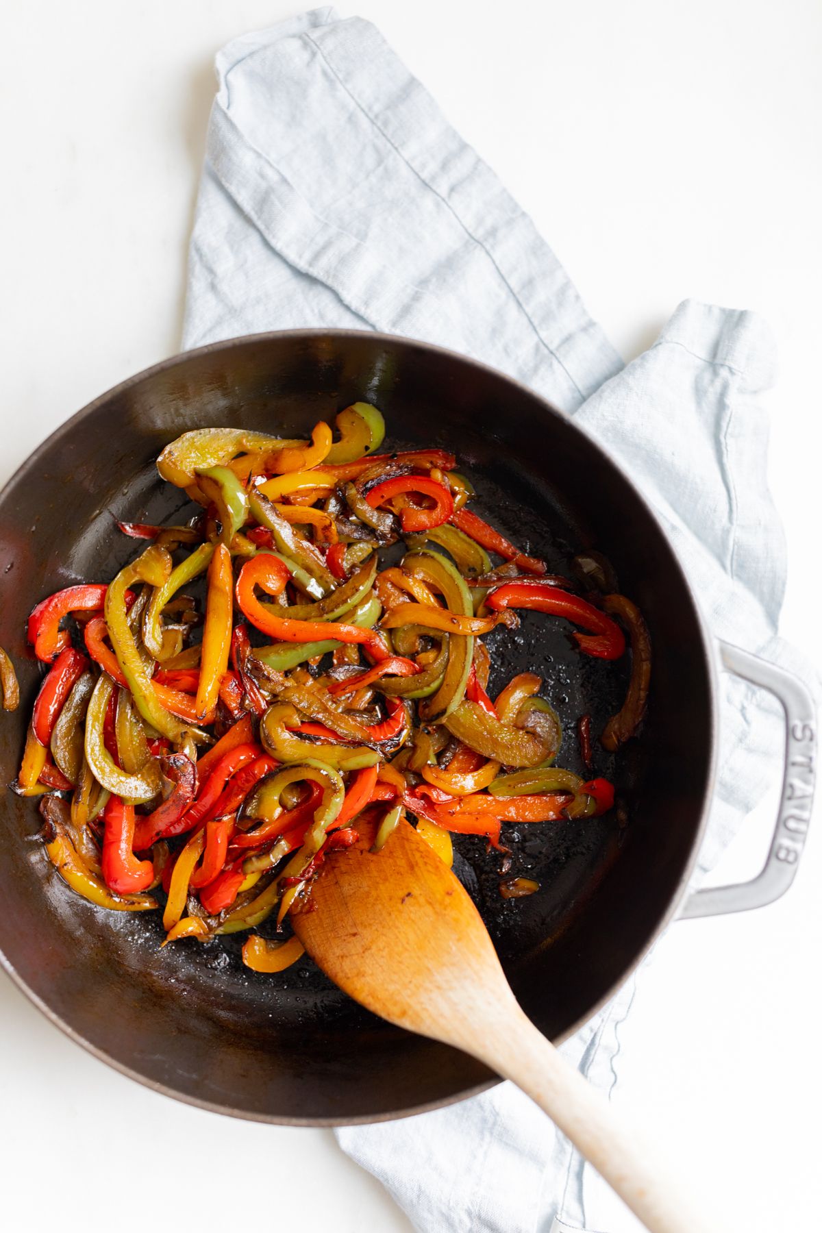 A cast iron pan full of sauteed bell peppers, wooden spoon to the side.