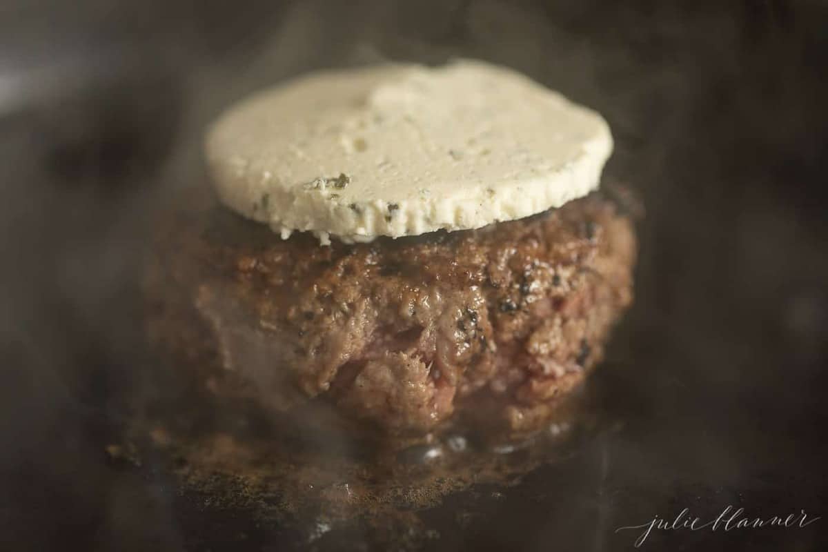 A burger in a cast iron pan, cooking with boursin cheese melting on top.