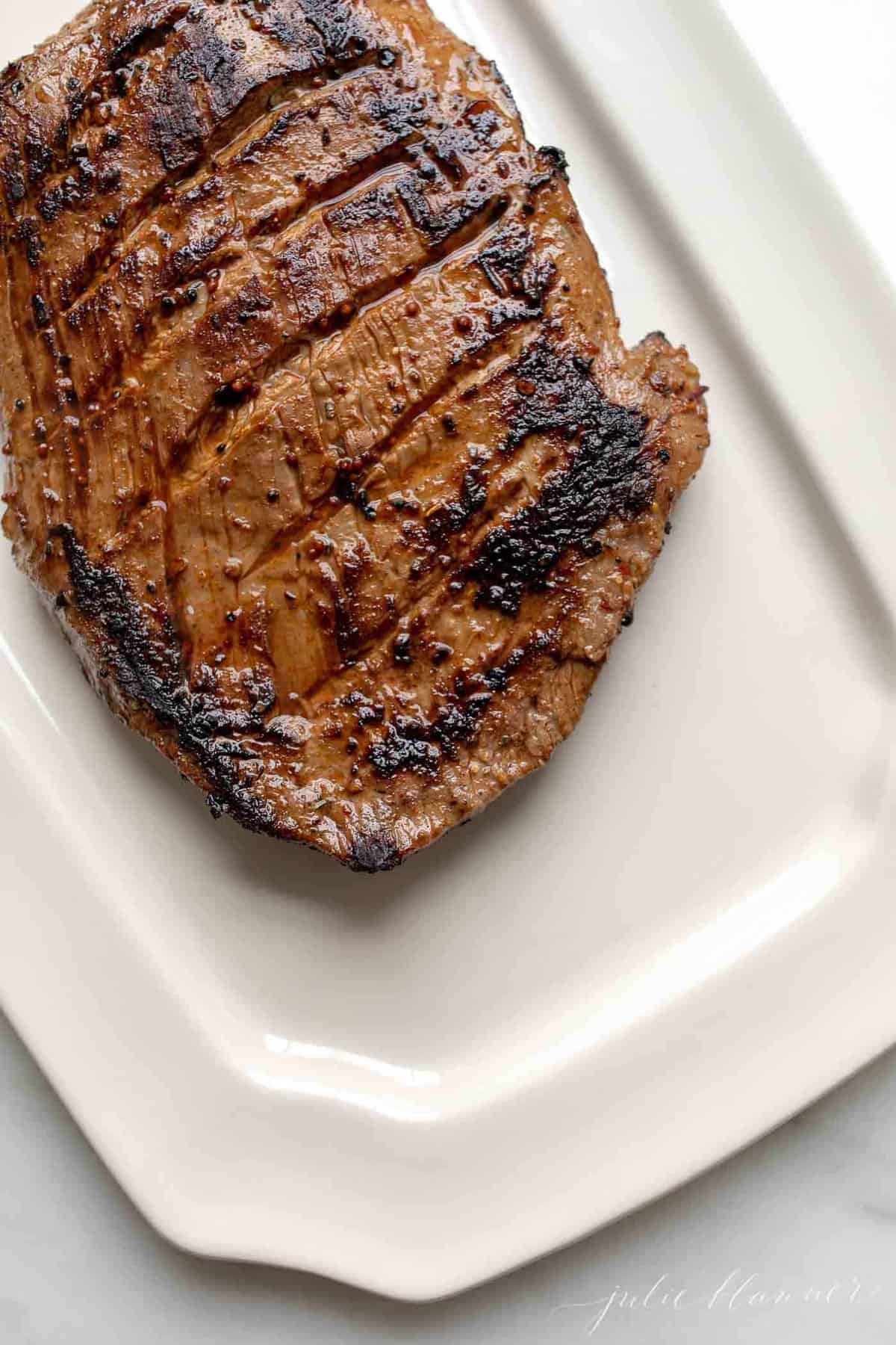 A white platter with a pan fried flank steak.