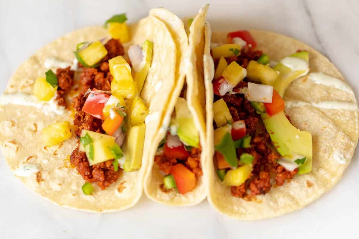 Three chorizo tacos in corn tortillas, on a marble countertop