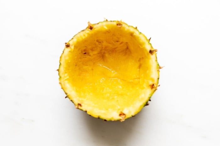 A pineapple, sliced in half with interior fruit removed, on a white surface.