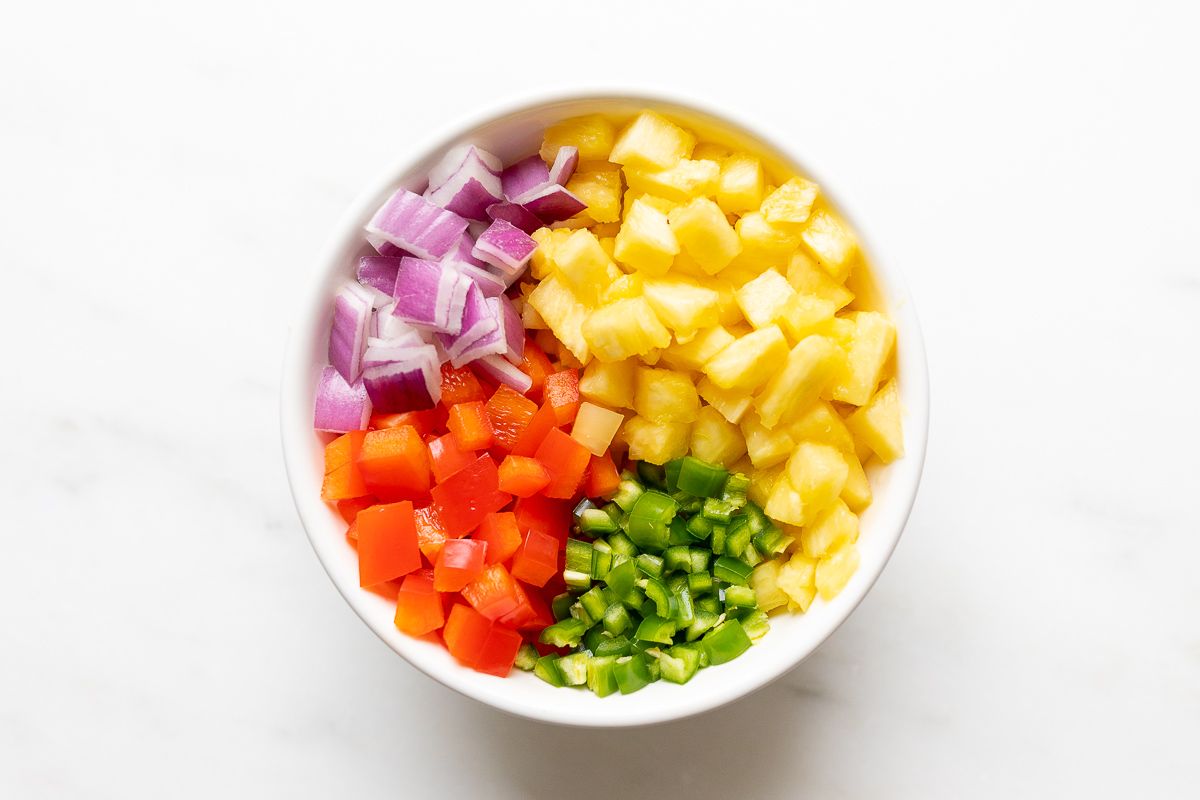 Ingredients for pineapple salsa, organized in a white bowl before mixing.