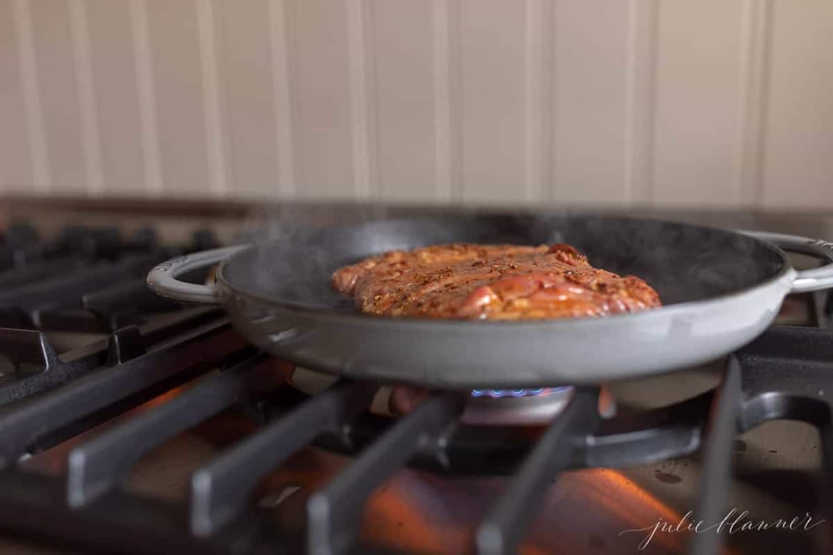 A cast iron pan on the stove, cooking flank steak.