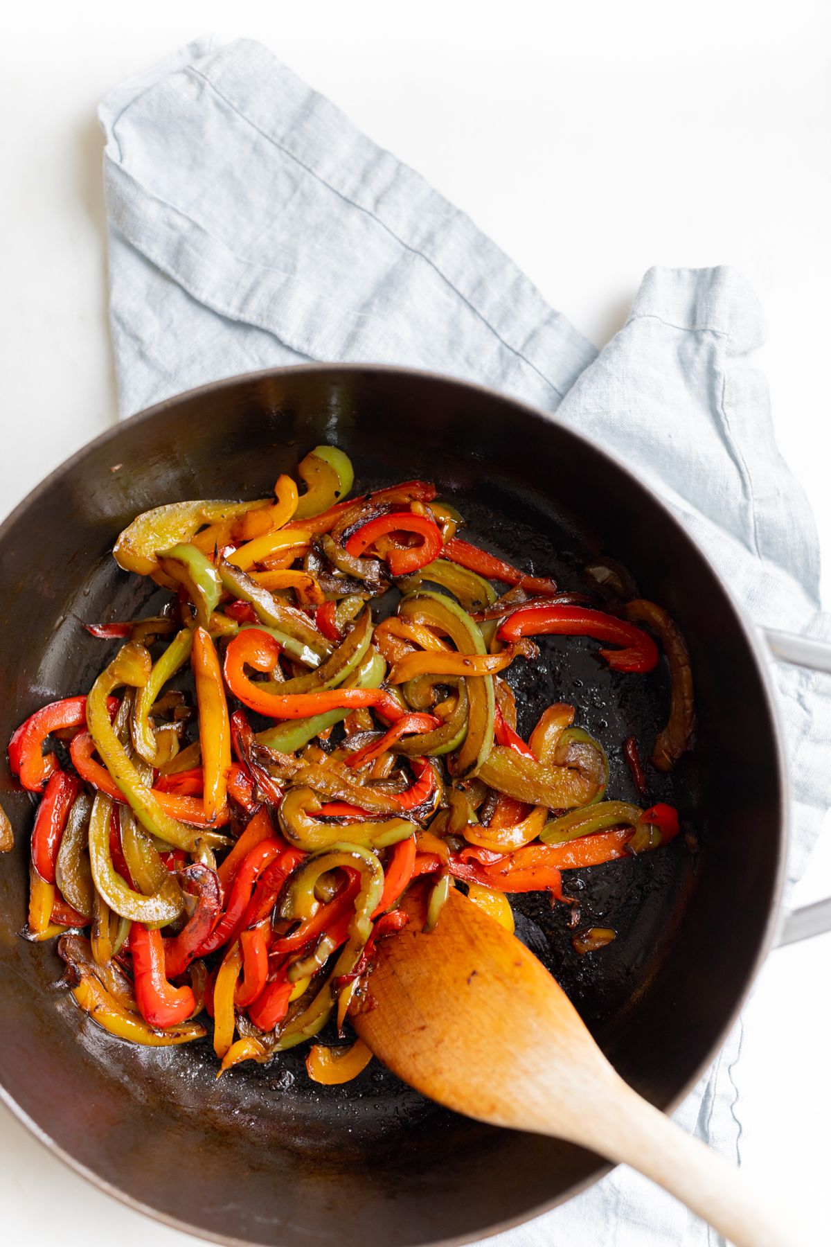 A cast iron pan full of sauteed bell peppers, wooden spoon to the side.