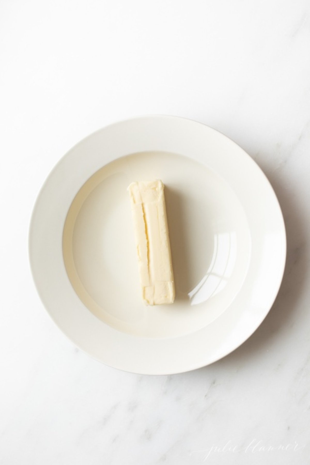 A single stick of butter on a white plate.