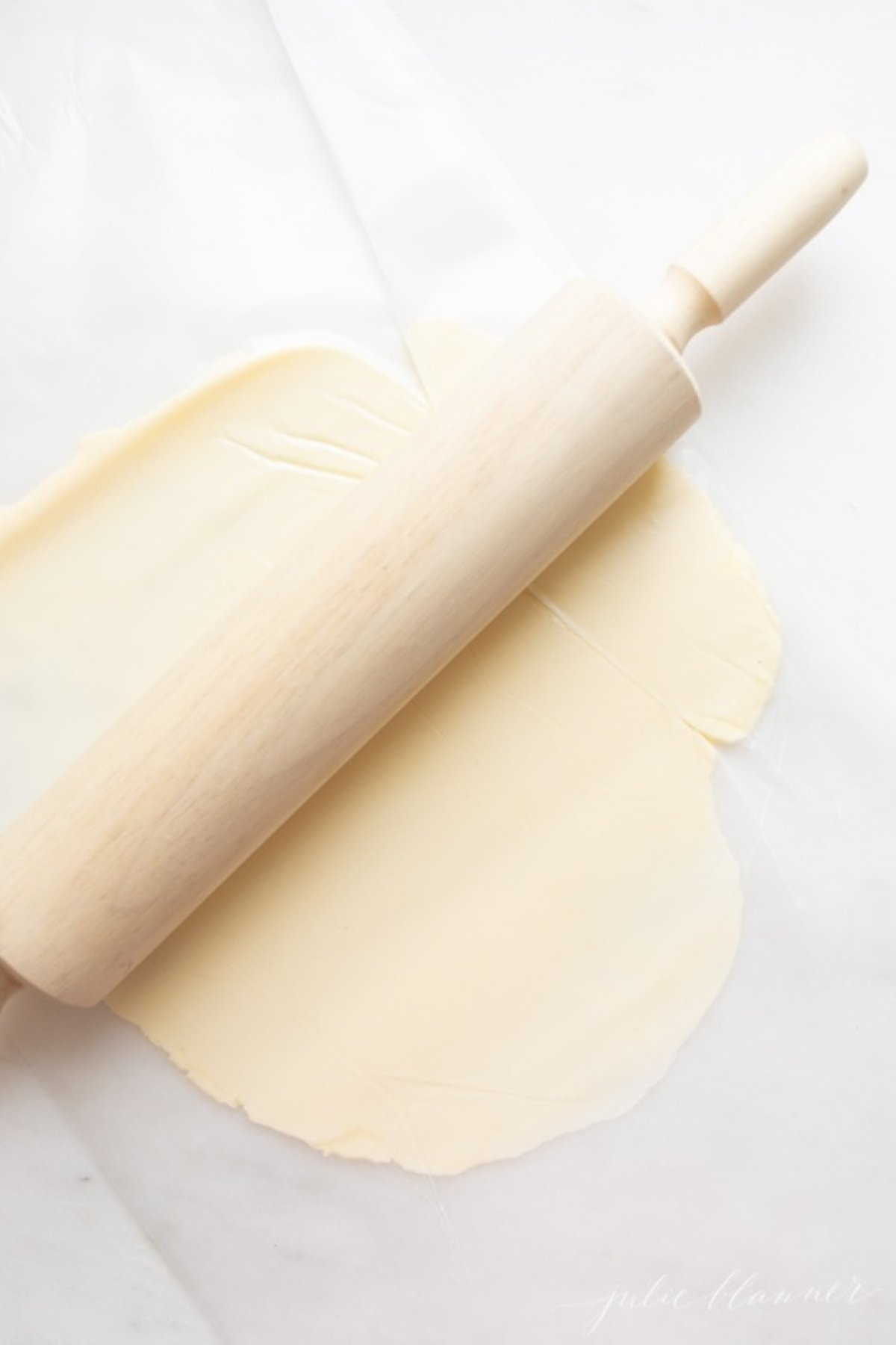 A wooden rolling pin next to a stick of butter that's flattened in between two sheets of waxed paper.