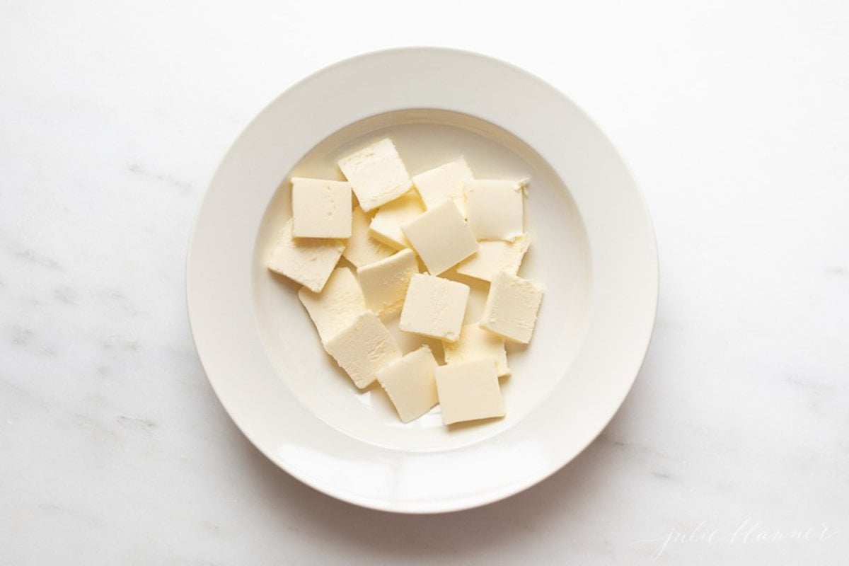 A white plate full of pats of butter in a tutorial for how to soften butter quickly.