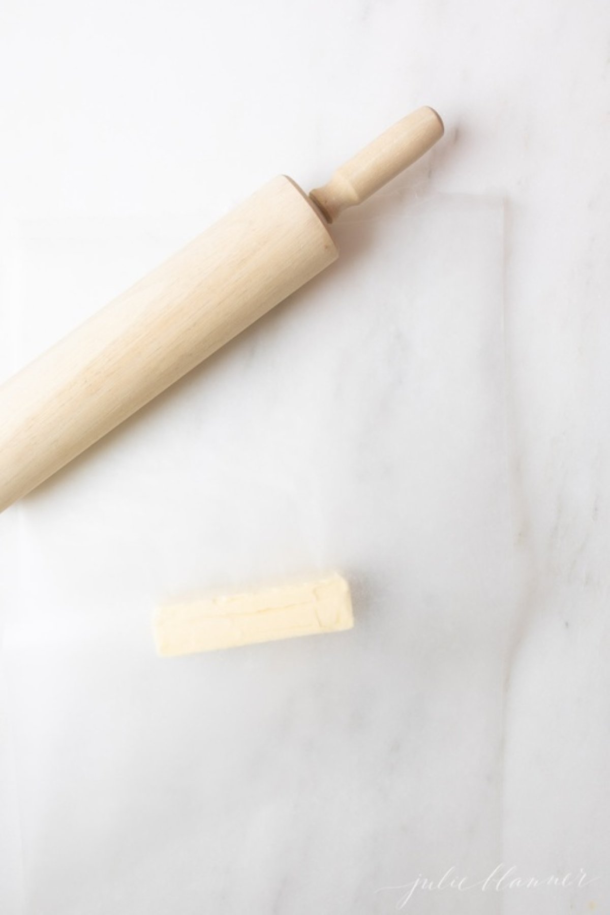 A wooden rolling pin next to a stick of butter that's placed in between two sheets of waxed paper.