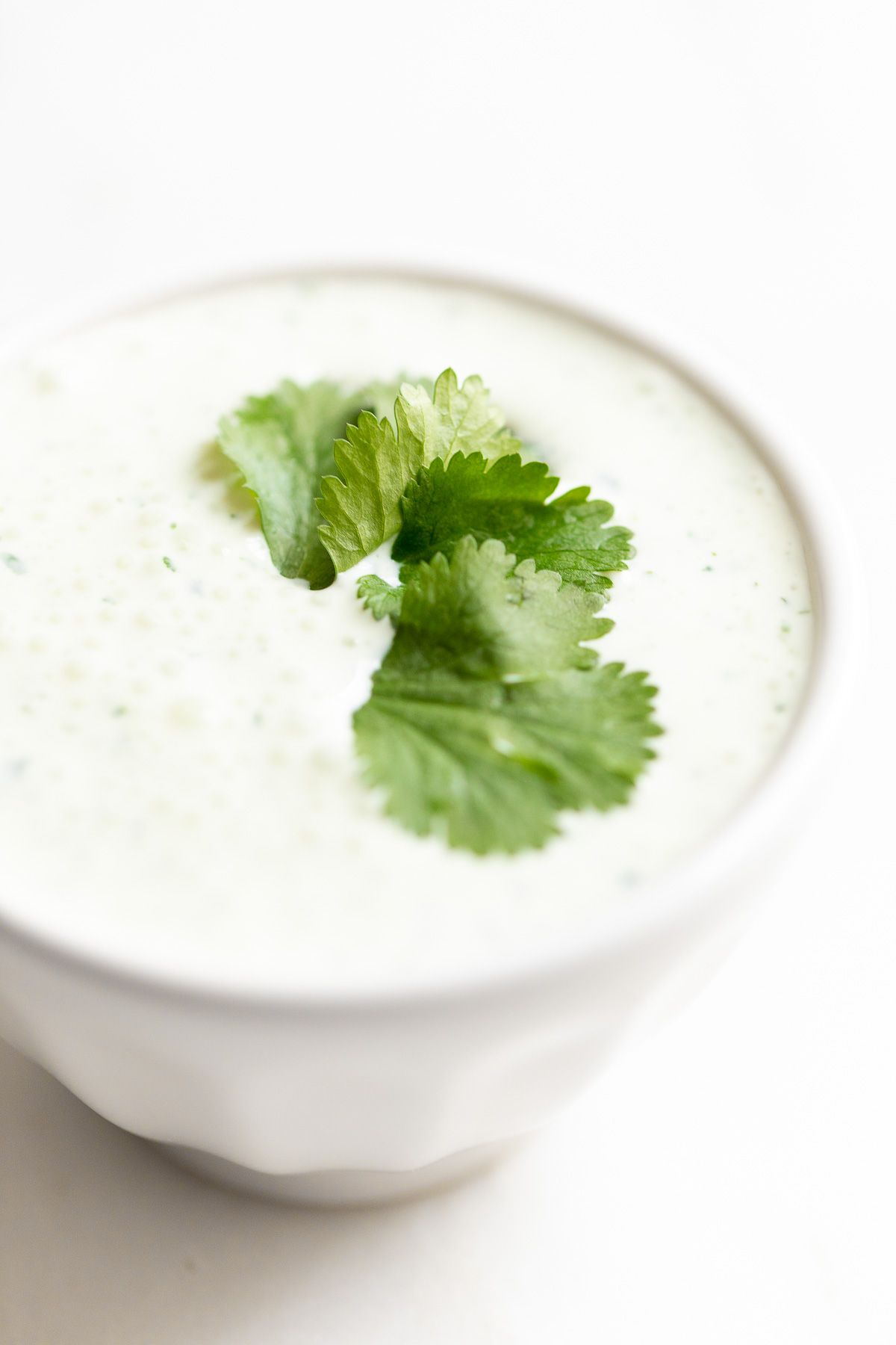 A white bowl of crema de cilantro on a white countertop, garnished with cilantro.