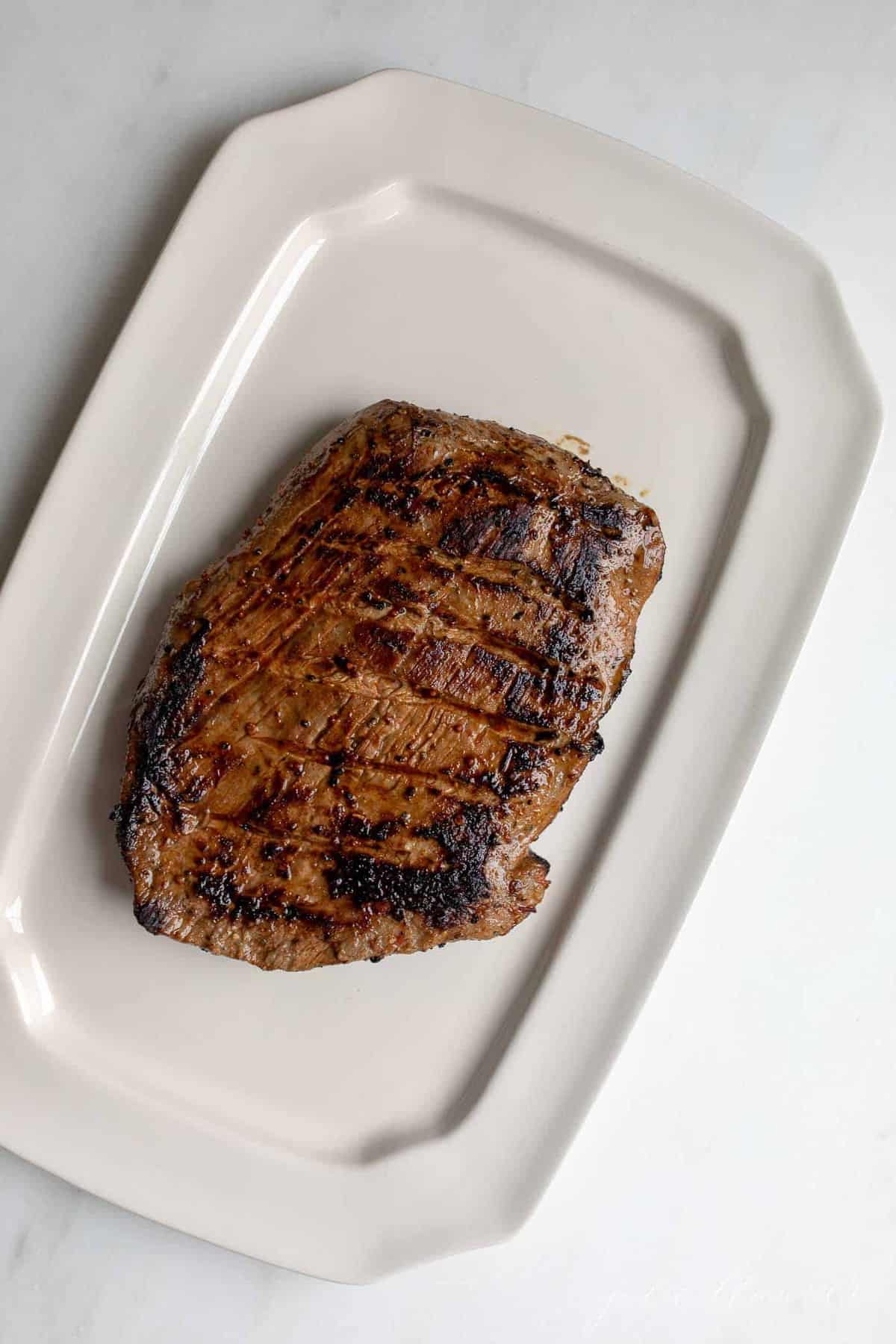 A white platter with a pan fried flank steak.