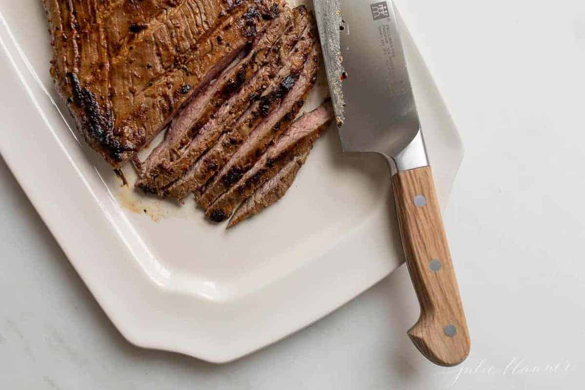 Steak being thinly sliced on a white platter. 