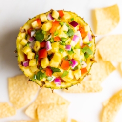 Pineapple salsa inside a pineapple bowl, on a white countertop. surrounded by tortilla chips.