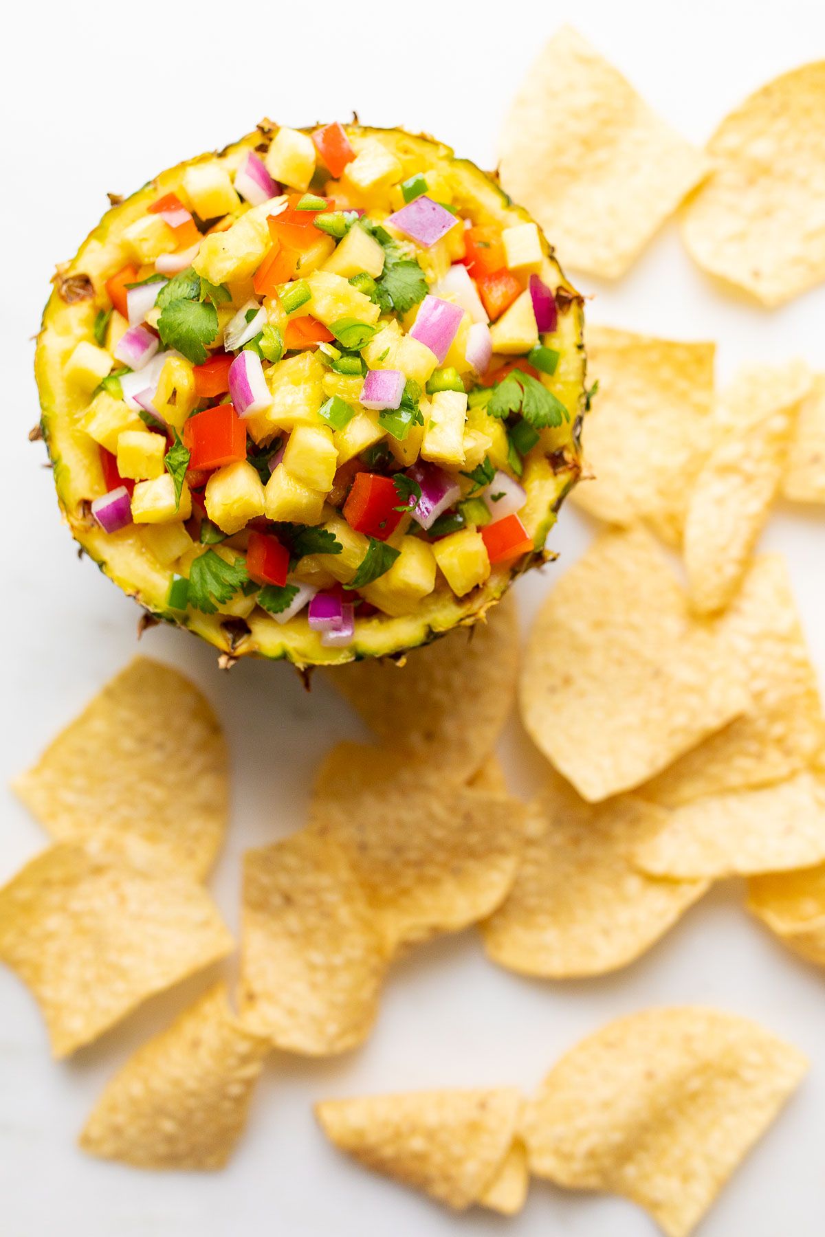 Pineapple salsa inside a pineapple bowl, on a white countertop. surrounded by tortilla chips.