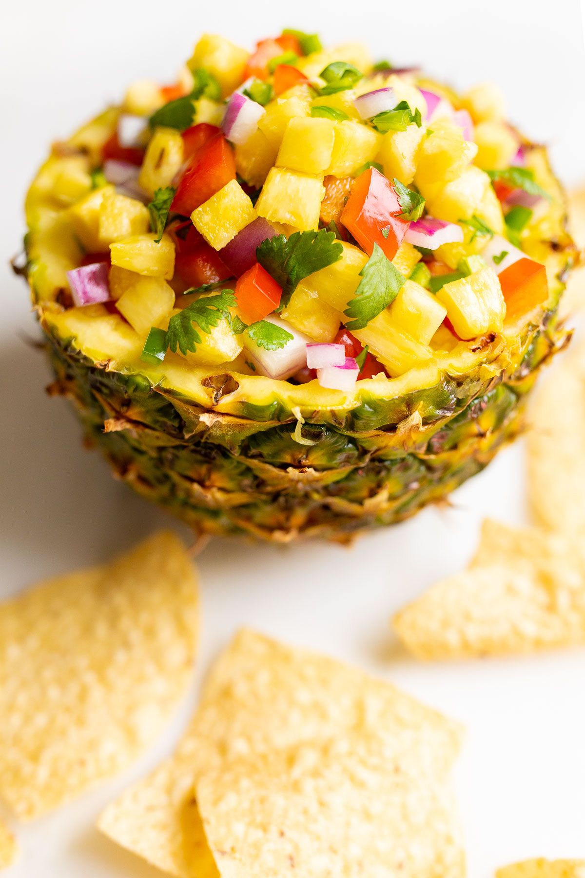 Pineapple salsa inside a pineapple bowl, on a white countertop. surrounded by tortilla chips.