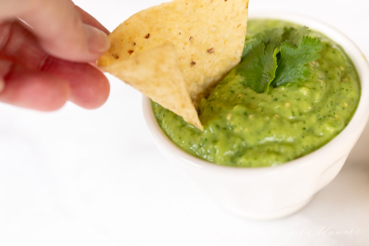 A hand dipping a tortilla chip into a bowl of salsa guacamole.