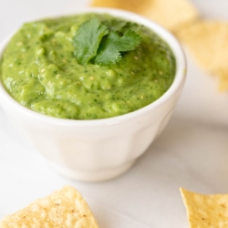 A white bowl of salsa guacamole surrounded by tortilla chips.